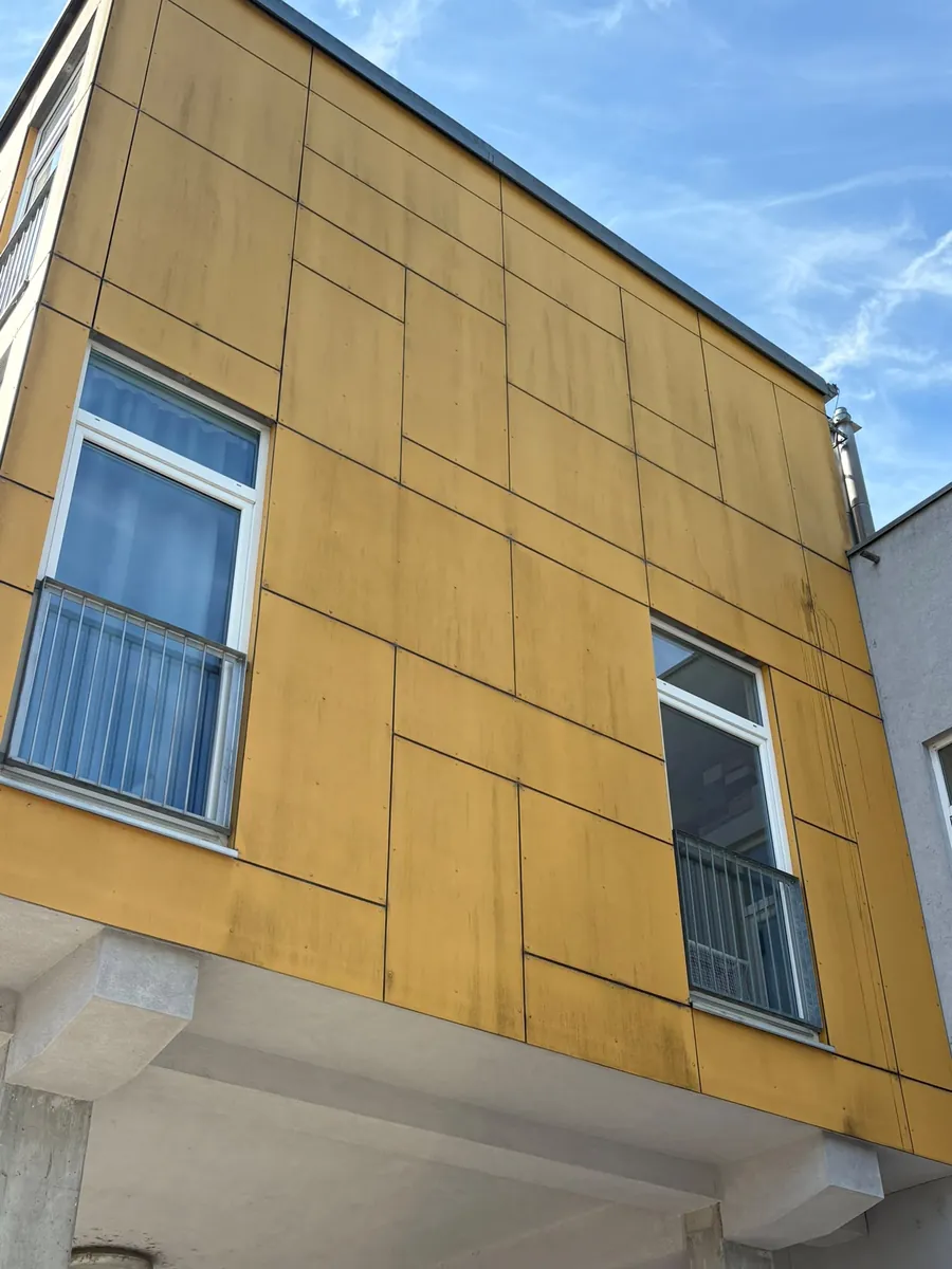 Gelbe Eternit-Fassade vor der Reinigung mit dunklen Verschmutzungen