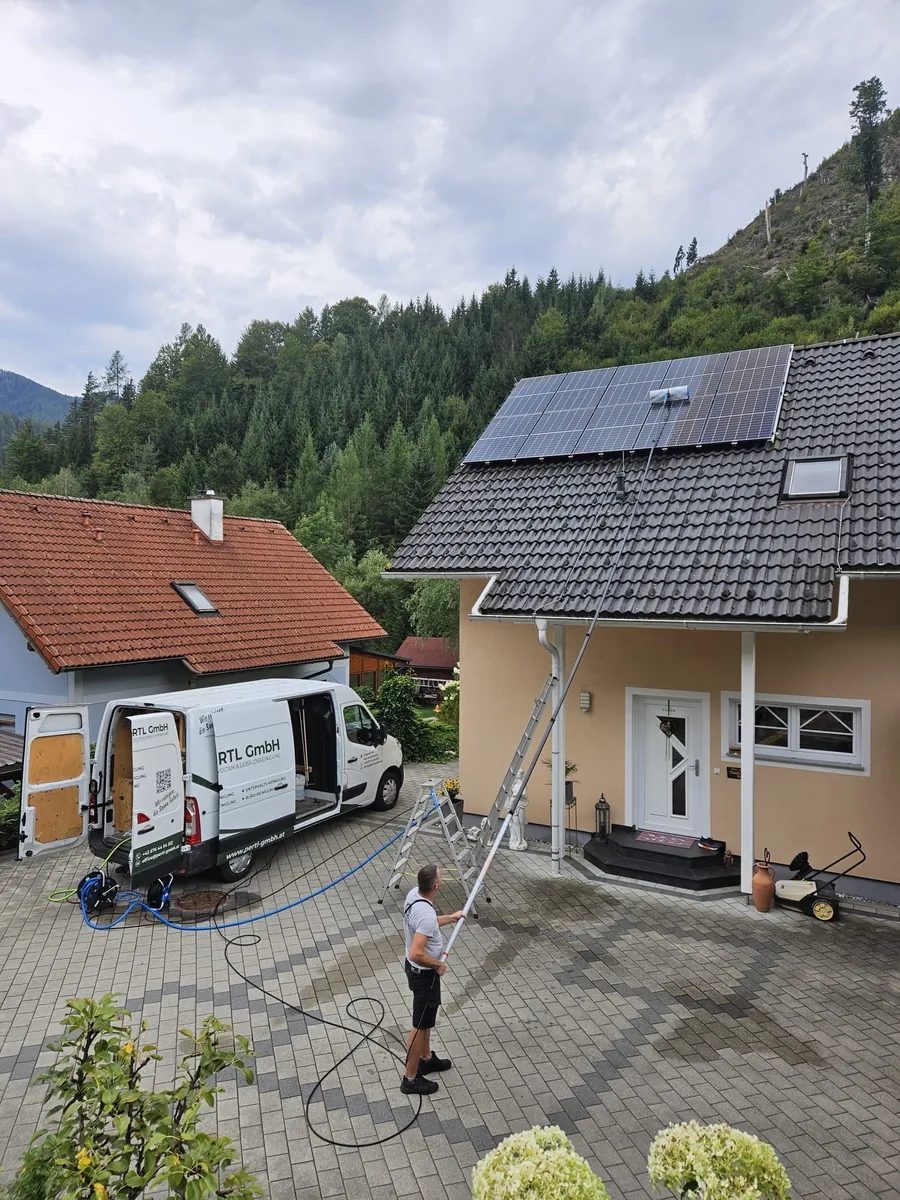 Photovoltaikreinigung auf einem Einfamilienhaus: Mitarbeiter von PERTL GMBH reinigt die Module mit Teleskopstange